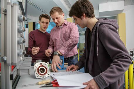 Drei Maschinenbau-Studenten tüfteln über Aufgaben im Labor. 