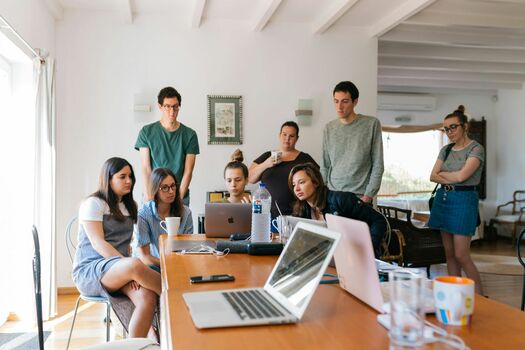 Ein Marketingteam tagt über eine Idee. Mehrere Personen schauen auf ein Laptop. Sie sprechen miteinander.